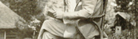 A black and white photograph of William Andrews Clark sitting on a wooden chair somewhere in an outdoor setting with trees in the background.