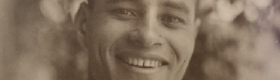 A black and white photograph of Ralph Bunche smiling, wearing a suit and tie, against a blurry background.