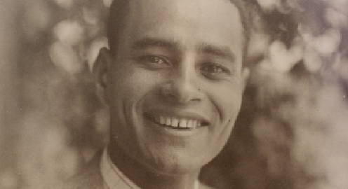 A black and white photograph of Ralph Bunche smiling, wearing a suit and tie, against a blurry background.