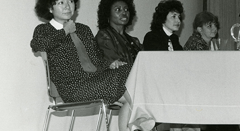 A black and white photograph of four women sitting a table as they look intently in front of them.