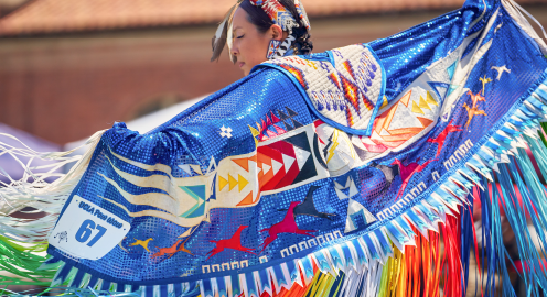 A woman in wearing a multi-colored Native American dress performing at a pow wow.