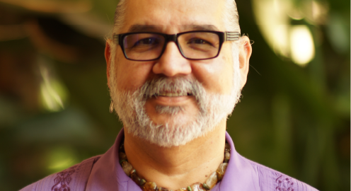 Alfred Herrera, the Center for Community College Partnerships' founder and now retired director, wearing a purple guayabera with a blurry outdoor setting in the background.