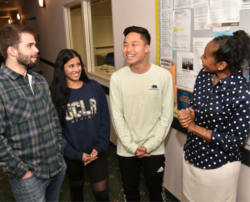 Angela Deaver Campbell, director of the Center for Scholarships & Scholar Enrichment, pictured here in a blue shirt with white polka dots in conversation with two males students and one female student in a hallway.