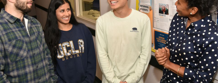 Angela Deaver Campbell, director of the Center for Scholarships & Scholar Enrichment, pictured here in a blue shirt with white polka dots in conversation with two males students and one female student in a hallway.