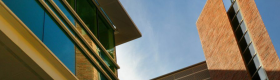 A skyward facing photograph of a building and a blue sky and clouds.