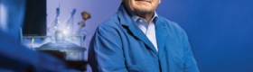 UCLA faculty Michael Jung wearing a blue coat sitting in a room with blue lighting next to a desk fashioned with lab equipment.