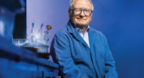 UCLA faculty Michael Jung wearing a blue coat sitting in a room with blue lighting next to a desk fashioned with lab equipment.