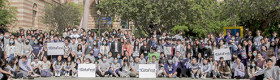 Nearly one hundred students participating in the American Statistical Association DataFest posing for a group photo in the courtyard with trees and a red brick building in the background.