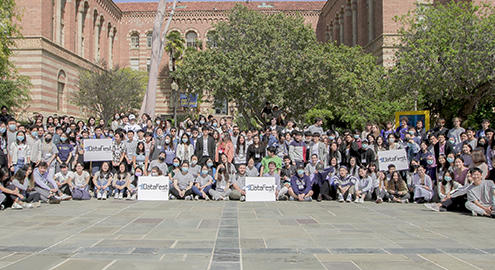 Nearly one hundred students participating in the American Statistical Association DataFest posing for a group photo in the courtyard with trees and a red brick building in the background.