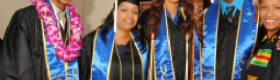 Two males and three female African American students in graduation regalia. From left to right, the students wear blue graduations sashes with golden accents; the student on the left wears a black sash with green, yellow and red decorative elements.