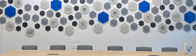 A wall in The Collaboratory, decorated with white, black and blue hexagons with a desk and chairs in front.