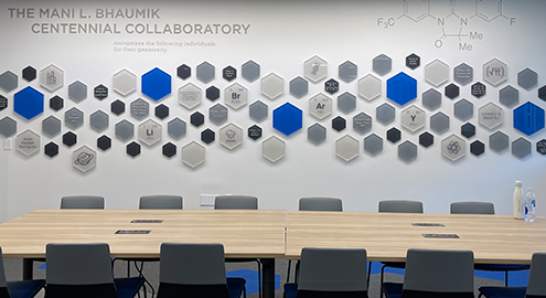 A wall in The Collaboratory, decorated with white, black and blue hexagons with a desk and chairs in front.