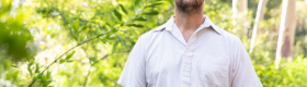 Park Williams in a white shirt standing outside with trees and green leaves in the background.