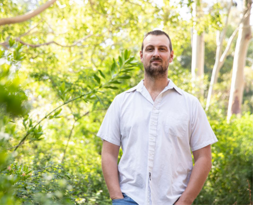 Park Williams in a white shirt standing outside with trees and green leaves in the background.