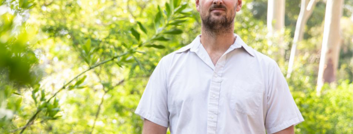 Park Williams in a white shirt standing outside with trees and green leaves in the background.