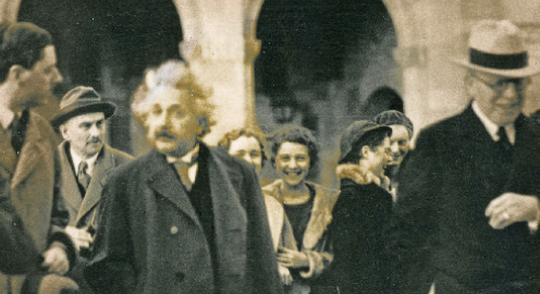 Albert Einstein surrounded by people with stone columns in the background.