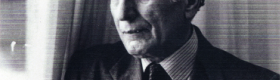 A black and white head and shoulders photograph of Ehsan Yarshater wearing a suit and tie and leaning against a window with curtains. Yarshater (1920–2018), served as the Hagop Kevorkian Professor of Iranian Studies at Columbia University and was a towering figure in the field.