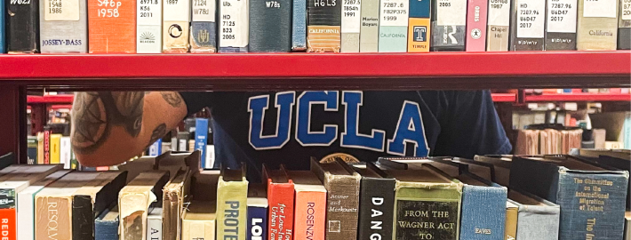 A photograph of a bookshelf with a person wearing a blue shirt that reads "UCLA" in the background.