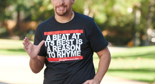 Adam Bradley standing outside on a sunny day, wearing a black shirt that reads: A beat at it's best is a reason to rhyme.