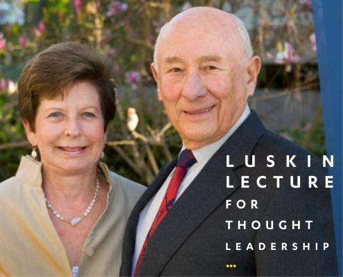 Meyer Luskin wearing a blue suit with a red tie and Renee Luskin in a beige dress with a pearl necklace standing outside with tree branches and pink and white flowers in the background.