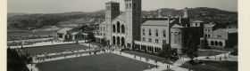 A black and white photograph of Royce Hall and students walking on a sidewalk, going to and from class.