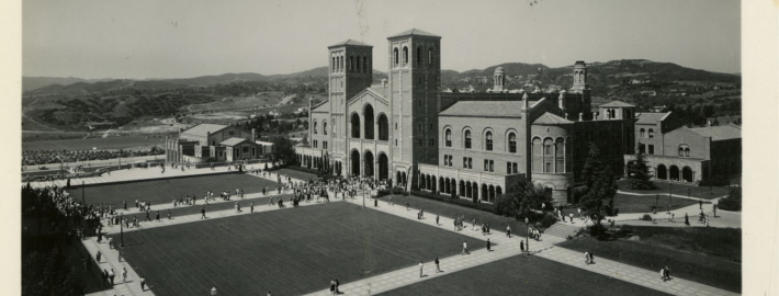 A black and white photograph of Royce Hall and students walking on a sidewalk, going to and from class.