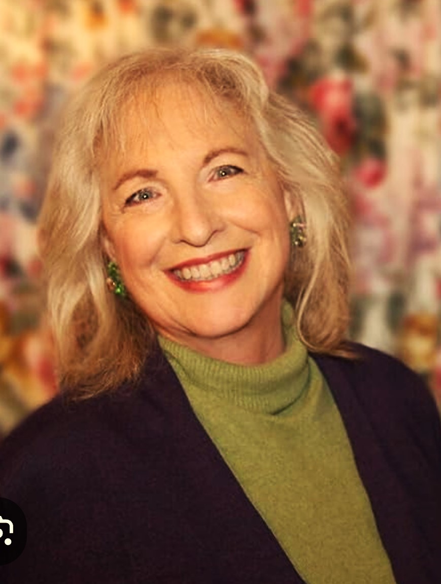 Jacqueline Braitman in a black sport coat and green turtleneck sweater against a blurred background.
