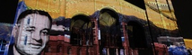 Image of a projection of Ralph Bunche's portrait and other colorful, UCLA Centennial-related images onto Royce Hall, against a night sky.