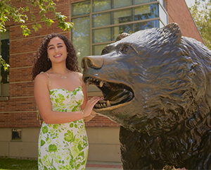 Catarina Gerges in a white dress with green flowers standing next to the Bruin statue.