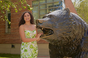 Catarina Gerges in a white dress with green flowers standing next to the Bruin statue.