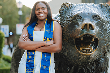 Naomi Hammonds wearing graduation sash, stands next to bear statue