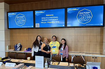 Four people stand below screen with 2023 UCLA National McNair Conference
