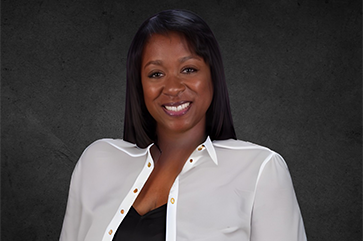 Sonya Brooks in a white blouse, smiling, against a dark graphite background.