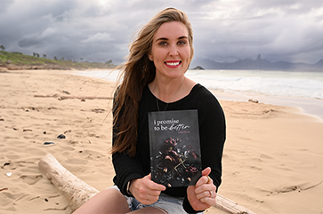 Erinn Keala holding a copy of her book on the beach.