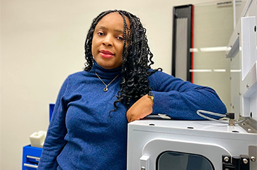 Professor Alvine Kamaha standing in front of instrumentation in her laboratory