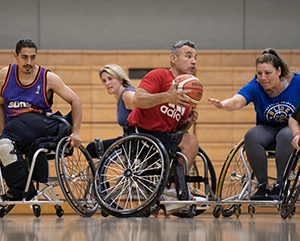 An action shot of five players who participate in UCLA Open Rec wheelchair basketball, with Alvin Malave holding the ball.