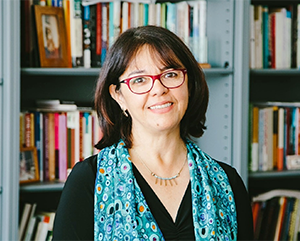 UCLA sociology professor Cecilia Menjívar stands in front of a full bookcase.