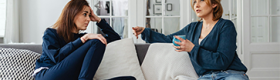 Two people speaking while seated on a couch.