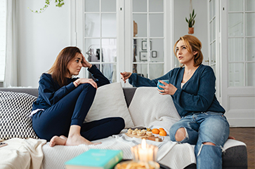 Two people speaking while seated on a couch.