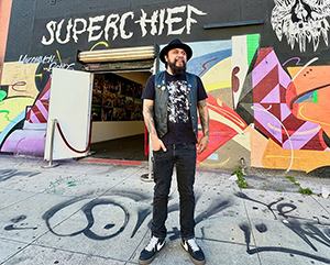 Erick Zerecero, dressed in black, standing in front of Superchief sign