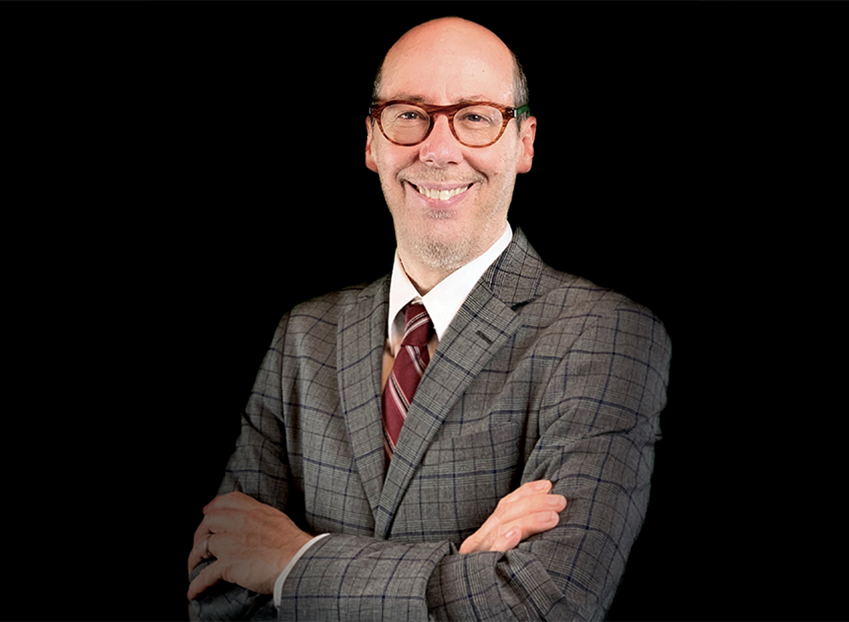 Jack Bobo in a grey suit and red tie against a black background. 