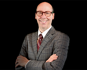 Jack Bobo in a grey suit and red tie against a black background.