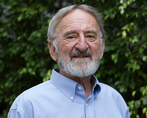 Keith Holyoak in a blue shirt standing in front wall with green leaves