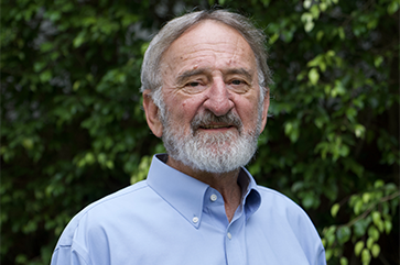 Keith Holyoak in a blue shirt standing in front wall with green leaves