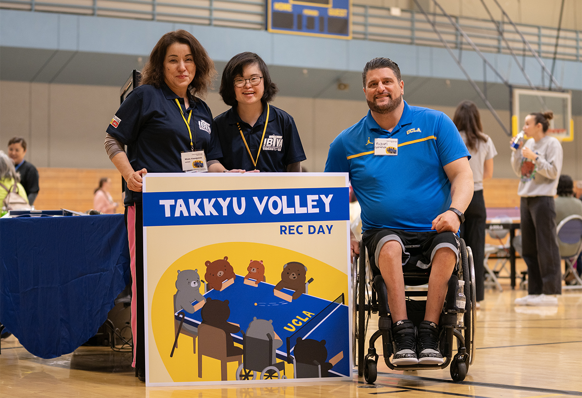 Michael Garafola (right) and two women posing in front of a poster for a Takkyu Volley event held on April 27, 2024. 