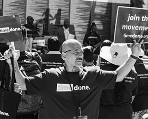 A man from the organization Time Done holds up a sign that reads ‘Join the Movement.’