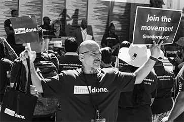 A man from the organization Time Done holds up a sign that reads ‘Join the Movement.’