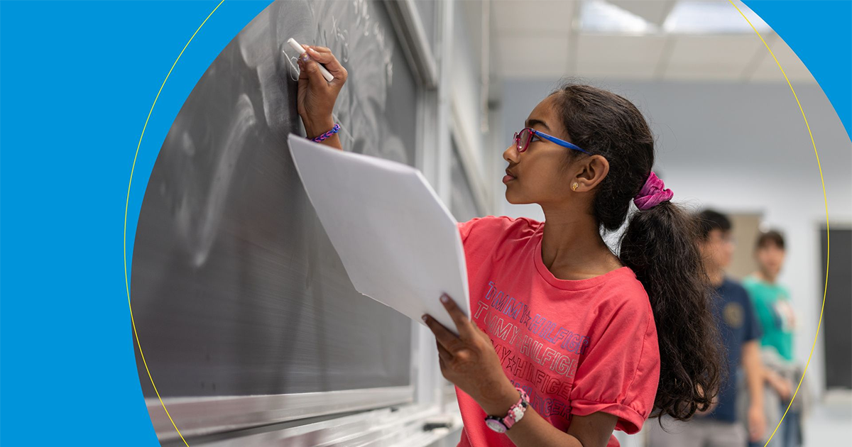 A young female student drawing math equations on a chalk board.