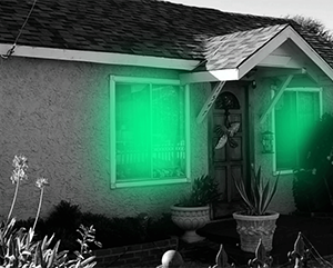 A black and white photo of a house with green light emanating from the windows.