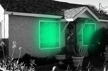 A black and white photo of a house with green light emanating from the windows.